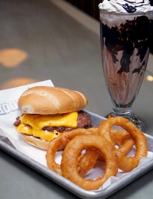 A burger with melted cheese, crispy onion rings, and a tall chocolate milkshake topped with whipped cream.