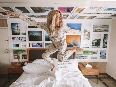 A woman yawns and stretches in a bedroom covered with beach-themed framed photos and paintings.