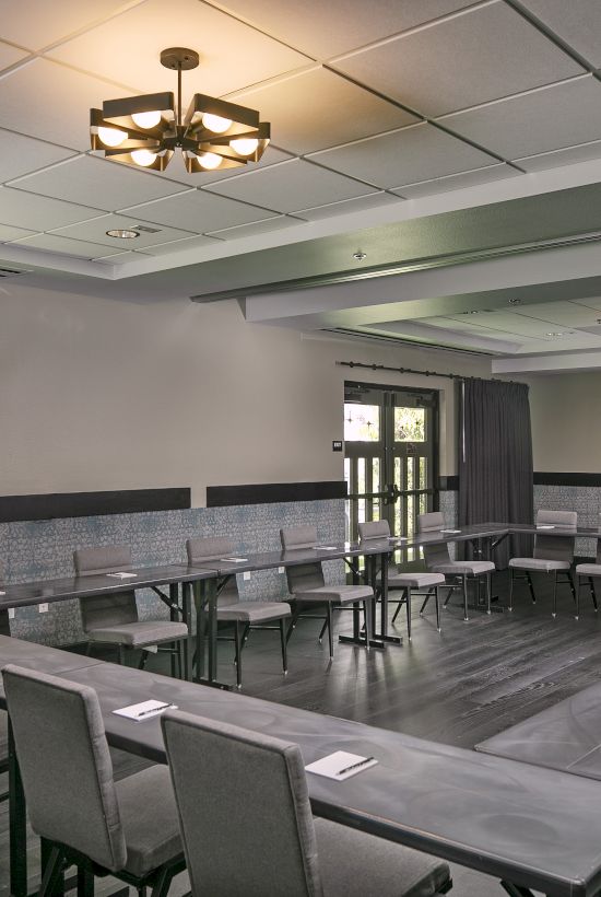 A bright conference room with rows of tables and chairs, ceiling lights, and a projector screen.